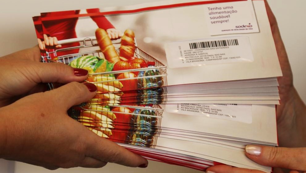 Imagem mostra mãos de duas pessoas, uma recebendo e outra entregando cartões do Mobiliza Campinas