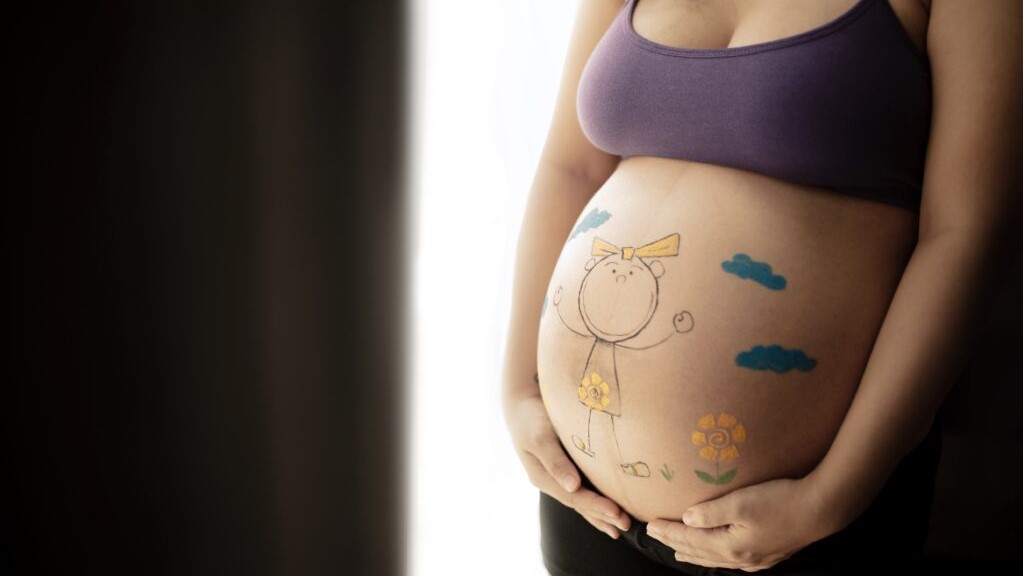 Barriga de uma mulher grávida. Desenhos infantis estão estampados na barriga.