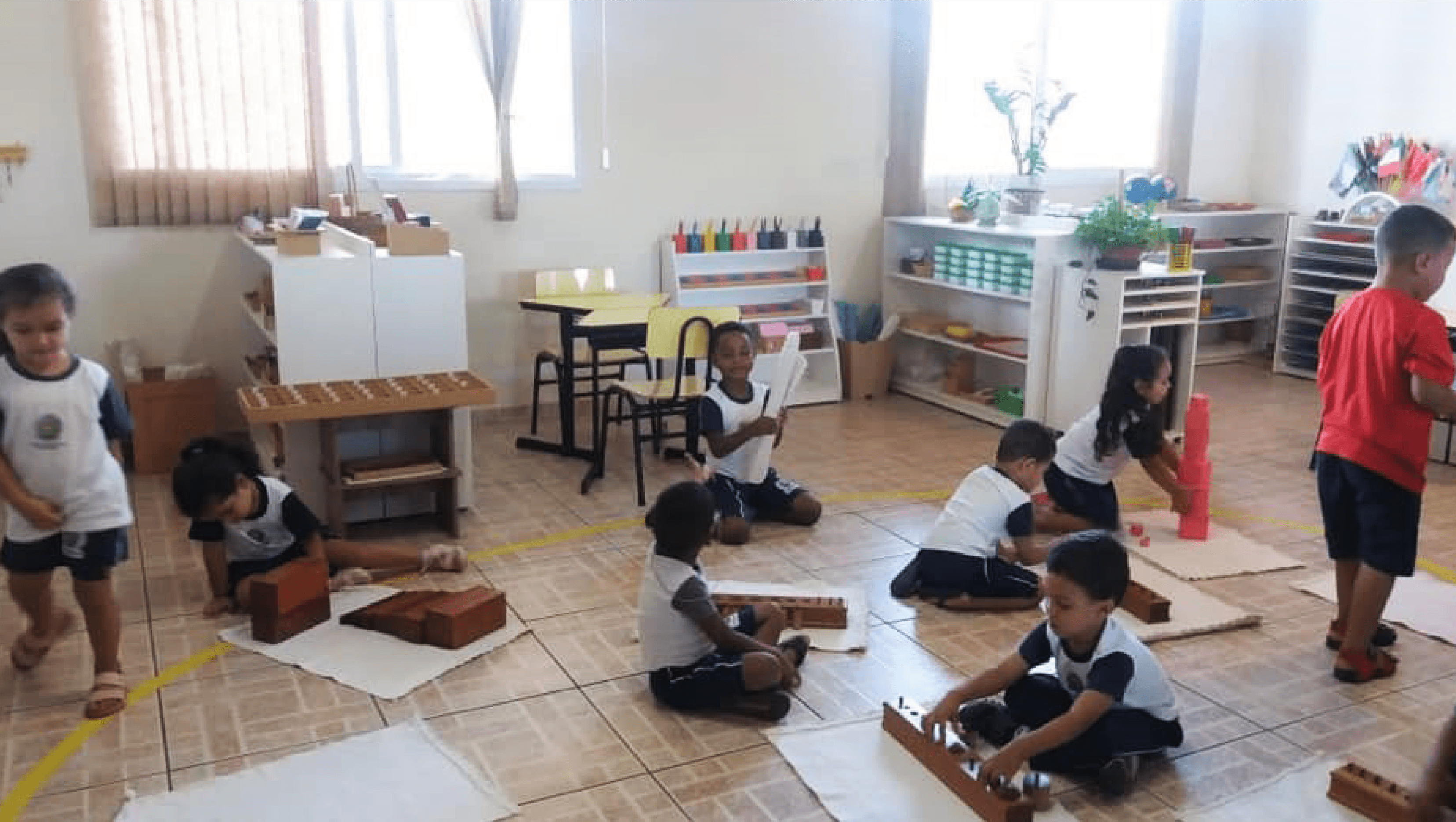 Imagem mostra crianças em uma sala de aula, sentadas no chão e interagindo com materiais lúdicos de aprendizagem