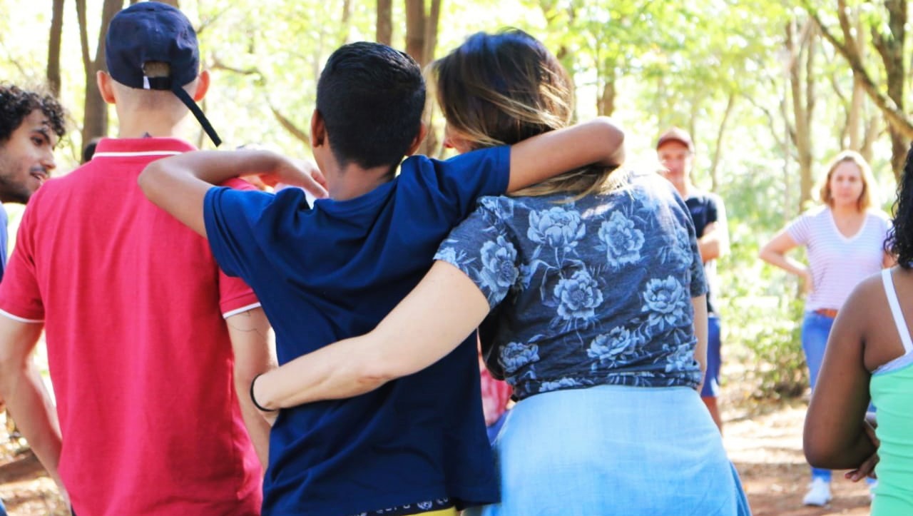 Imagem mostra mentora e jovem abraçados em um ambiente externo, durante encontro promovido pelo projeto Trilhar
