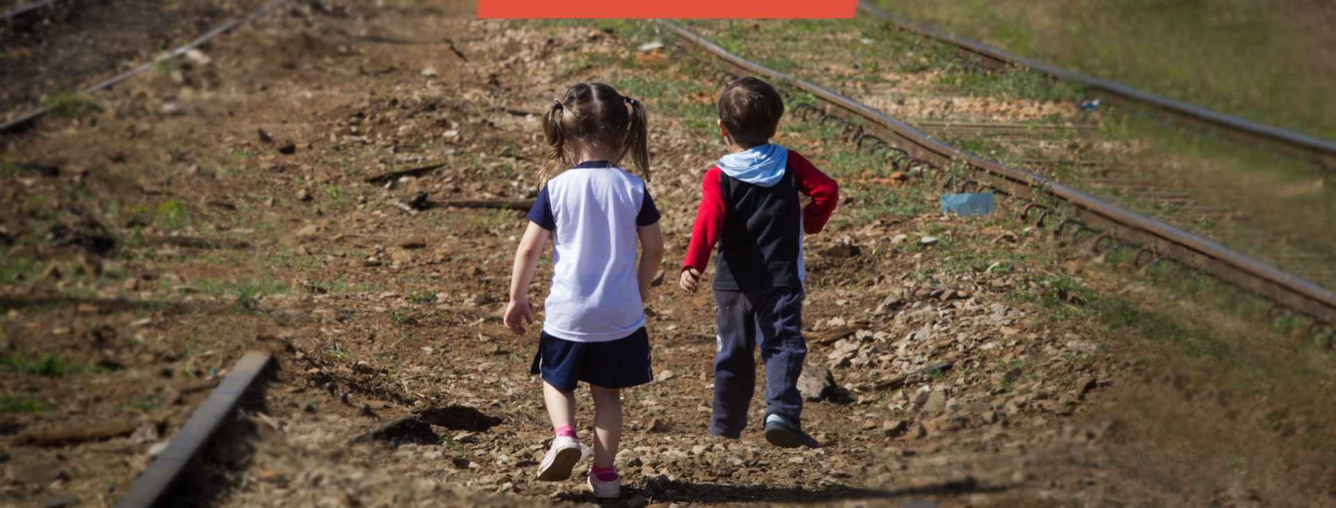 Foto de duas crianças de costas, caminhando sobre um caminho de terra