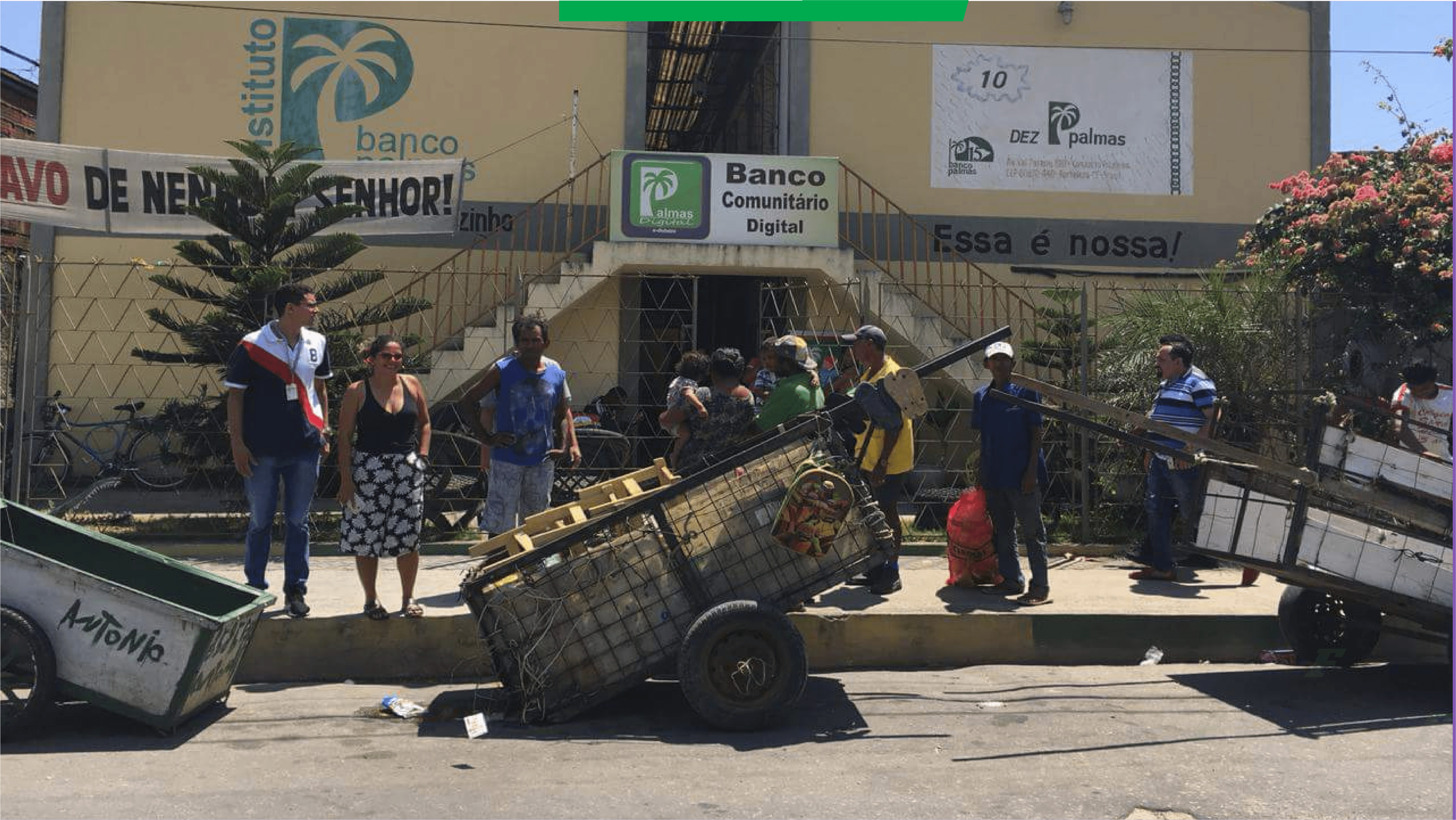 Três carroças e algumas pessoas estão paradas na frente de um prédio do Instituto Banco Palmas no qual há uma placa escrita banco comunitário digital.