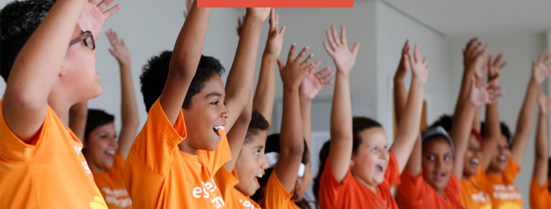 Grupo de crianças, vestindo camiseta laranja, comemorando felizes com as mãos esticadas para cima