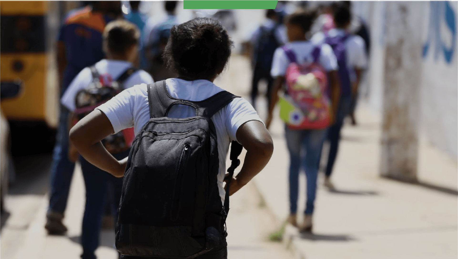 Criança de costas carregando mochila à caminho da escola