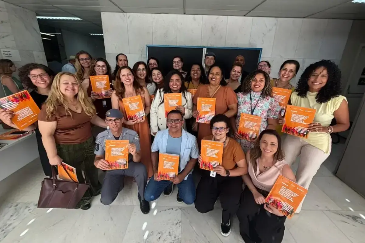 Grupo de pessoas sorridentes posando para foto segurando o exemplar do guia de implementação de fluxos de atendimento a crianças e adolescentes.