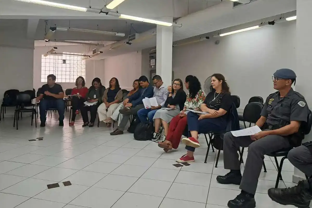 Cerca de 12 participantes sentados em cadeiras dispostas em semicírculo em sala ampla, incluindo um policial militar fardado, durante oficina do CAI de implementação da Lei Escuta Protegida.