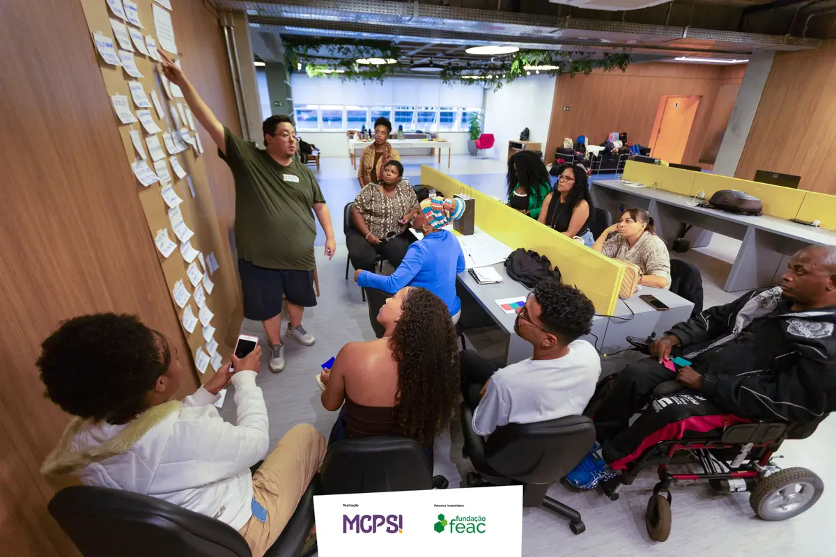 Facilitador do LabPOP apresenta ideias em um mural com diversos post-its para o grupo em um espaço de trabalho colaborativo.