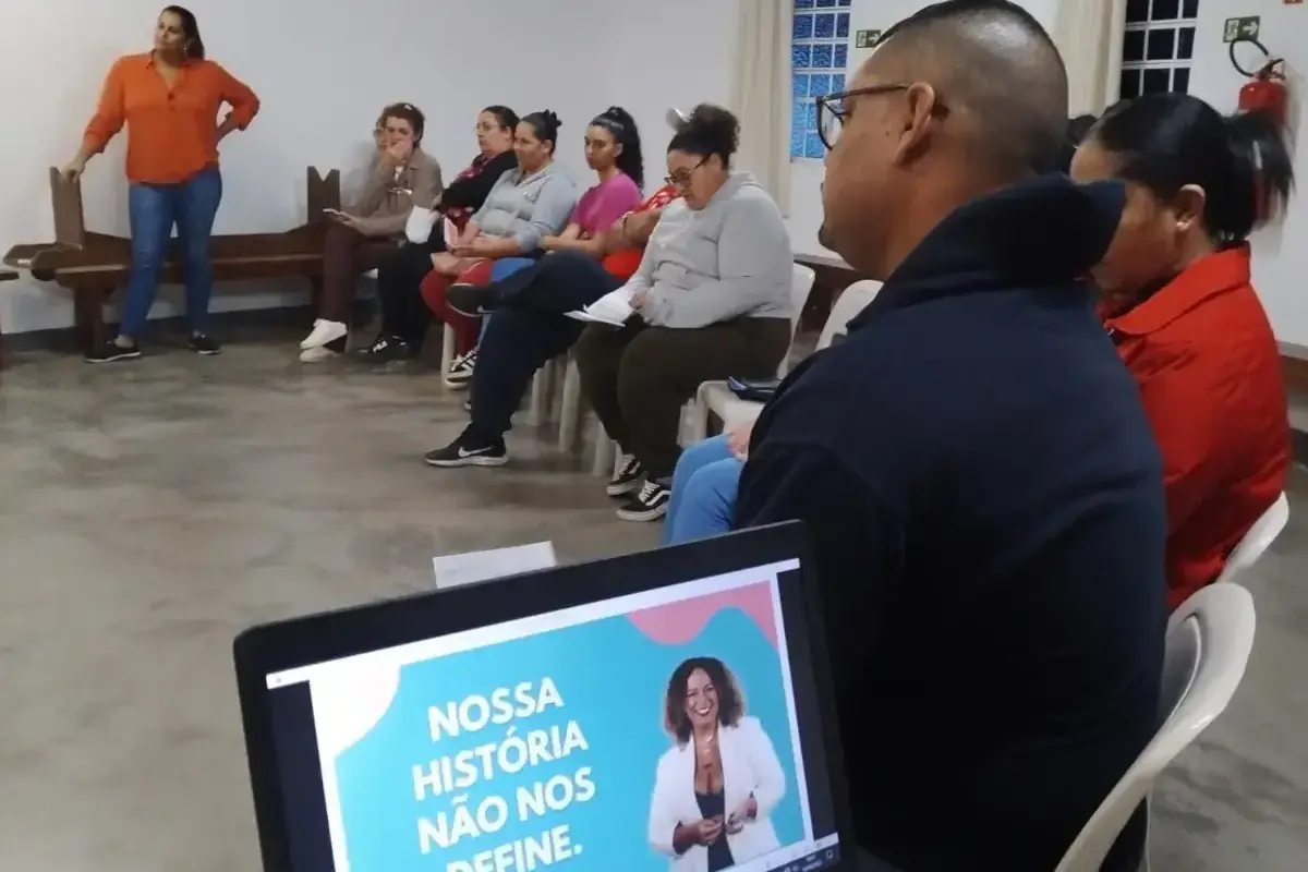 Roda de conversa com pessoas sentadas em círculo, com um notebook em primeiro plano exibindo uma apresentação motivacional.